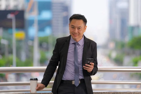 Азиатский бизнесмен стоит и держит мобильный телефон с бизнесом — стоковое фото