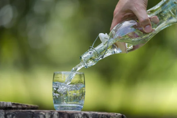Ruční nalévání pitné vody z láhve do skla s přírodní bac — Stock fotografie