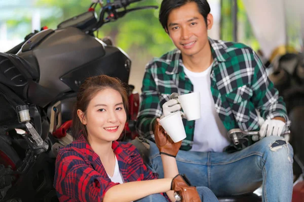 Happy couple drinking coffee at a motorcycle repair shop — Stock Photo, Image