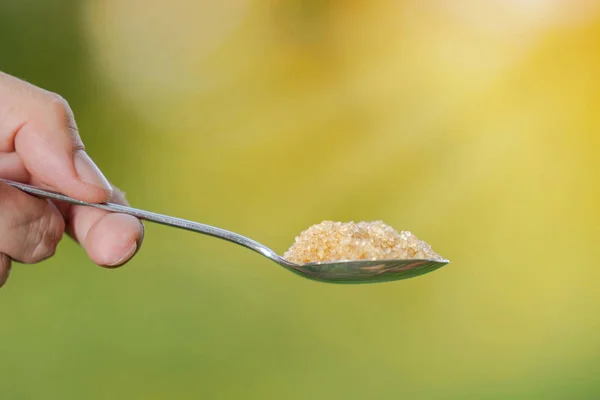 Hand hält einen Löffel mit Zucker auf natürlichem Hintergrund — Stockfoto