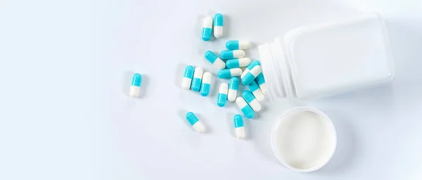 Blue and white capsules pills pouring from the bottle on white b — Stock Photo, Image