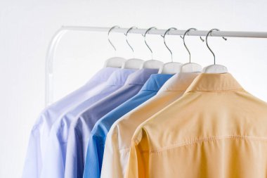 Erkeklerin gömleklerini kapatın, beyaz arka planda askılarda giysiler