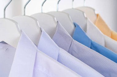 Erkeklerin gömleklerini kapatın, beyaz arka planda askılarda giysiler