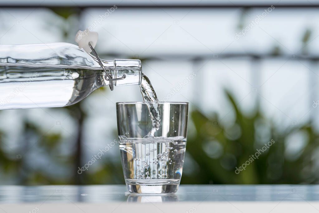 Pouring drink water from bottle into glass at garden home