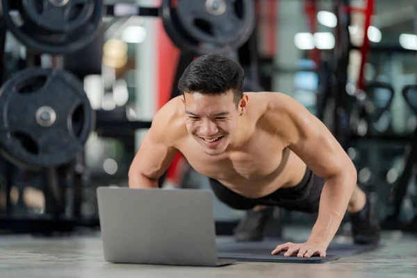 Online training, Sport man training doing push-ups exercise with laptop in fitness gym