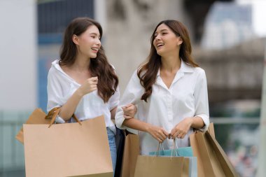 Mutlu arkadaşlar alışveriş yapıyor, iki genç bayan alışveriş torbaları tutuyor, genç kadınlar şehirde alışveriş yapıyor.
