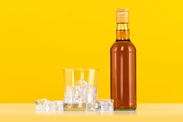 带冰块的威士忌和黄色背景的瓶子 — 图库照片