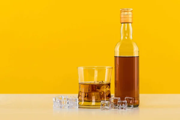 带冰块的威士忌和黄色背景的瓶子 — 图库照片