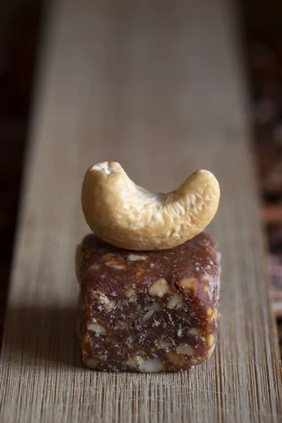 Natural vegan organic sweets made of dried fig, cashew nuts and peanut. Fruit and nuts candy bar with the whole cashew nut on the top on wooden board and wicker tray.