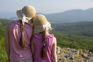Dantel kurdeleler ile güzel yaz saman kapaklar iki küçük sevimli kız arka görünümü birlikte duruyor ve Ghost vadisi ve Karadeniz, Kırım yakınındaki dağlarda güzel manzara bakıyor.