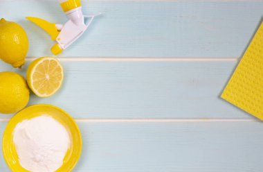 Eko temizlik için doğal ürünler. eko temizlik için limon, kabartma tozu ve sirke. Tüm nesneler, limon, kase, yıkama süngeri, pompa püskürtücü sarı renktedir. Mavi ahşap arka plan.