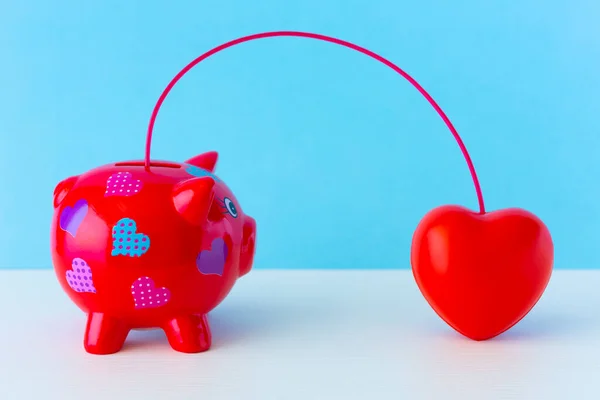 Blood Donor Day concept. Piggy bank and red heart connected by a vessel. Blood donation.