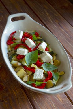 Ratatouille, ahşap arka planda beyaz fırın tavasında beyaz fesleğen ve peynirli sebze..