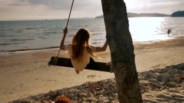 Yavaş hareket içinde bir tropikal plajda bir salıncak üzerinde genç kadın