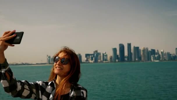 Tourist girl taking selfie photos at the skyscrapers with smartphone in doha — Stock Video