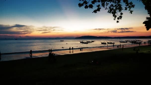 Pessoas na praia ao entardecer com barcos atrás — Vídeo de Stock