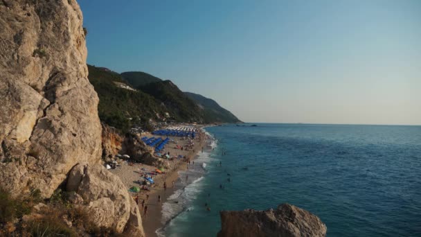 俯瞰美丽的海滩和海岸线 游客们在波涛中嬉戏 还有许多雨伞和日光浴床 — 图库视频影像