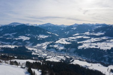 Bir dron görünümünden bir küçük köy kış dağlar arasında orman ve kar ile kaplı.