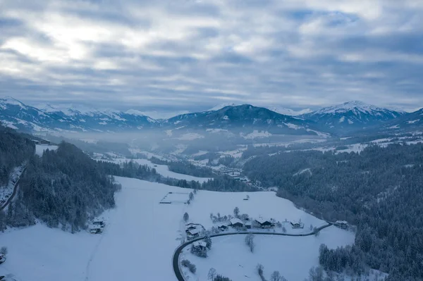 Ранковий туманний верхній панорамний вид на сніг і село з деревами і дорогу на зимовому ландшафтному тлі гірських альп . — стокове фото