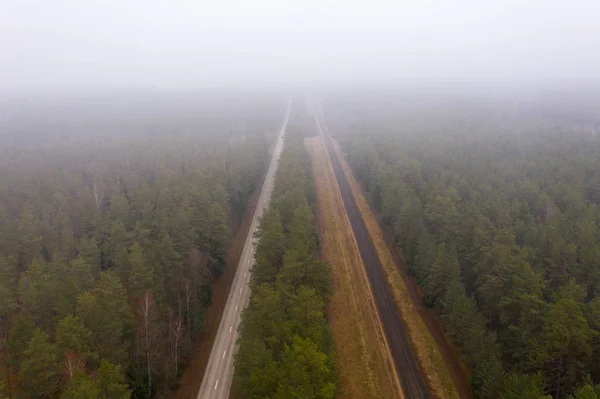 Drone view of forest, road and railway during cloudy day in rural landscape.