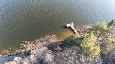 Ağaçlarla çevrili sakin bir göle uzanan ahşap bir rıhtım manzarası..