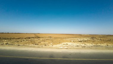 Açık mavi gökyüzü ve boş yolu olan engin bir çöl manzarası. Suriye