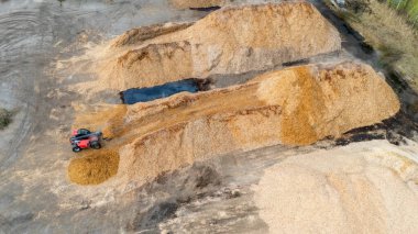 Kırmızı yükleyicili ahşap çip yığınlarının hava görüntüsü.