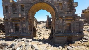 Kayalık arazi ve açık mavi gökyüzü ile çevrili kemerli antik taş kalıntıları. Antik Dara şehri, Suriye.