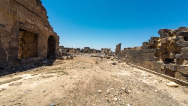 Açık mavi gökyüzünün altında taş duvarları ve kemerli antik kalıntılar. Antik Dara şehri, Suriye.
