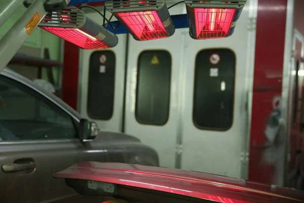 detail of the car body is drying under the lamps after painting. red lamps for drying painted parts are switched on in the service station