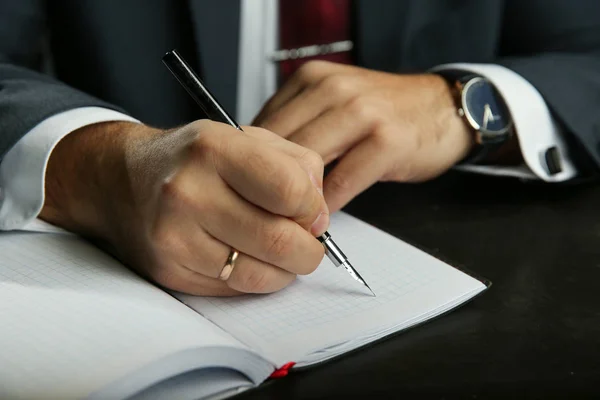 Businessman\'s hand writes with fountain pen. the lawyer signs the document with a fountain pen closeup. the hand of a man in a business suit writes with a pen in a diary.