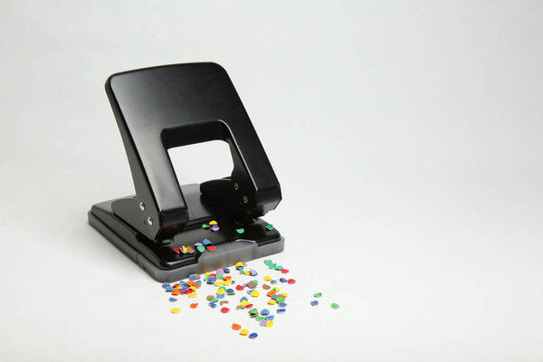black office hole punch with confetti isolated on white background.  Hole puncher sprinkled whith colorful confetti. 