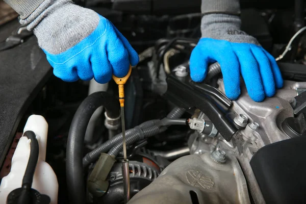 mechanic\'s hands in gloves check the oil level in the car. car mechanic pulls the dipstick the oil from the engine of the car