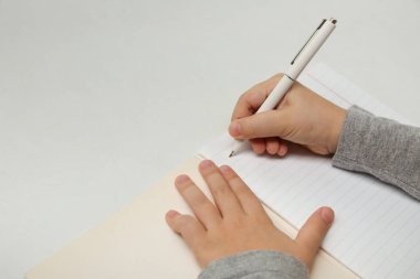 Çocuğun eli beyaz arka planda bir defter yazıyor. Çocuk ilk harfleri yazar. Beyaz arka planda bir çocuğun elinde beyaz kalem.