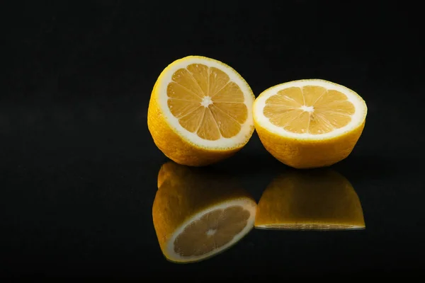 two halves of lemon on a black background close up with reflection. citrus fruit isolated  on black background