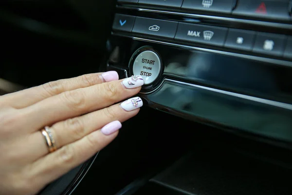 female hand presses the start button the engine in the car close up. women\'s fingers with beautiful manicure start engine of the luxury car