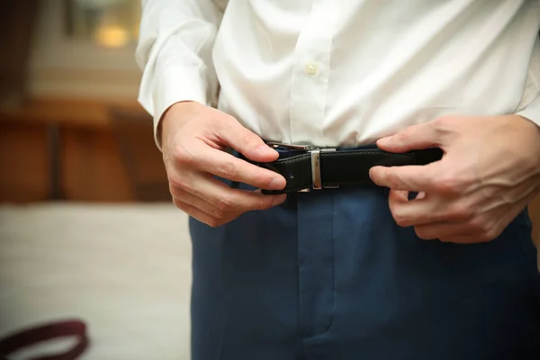 the man tuck the belt in the pants. men hands are putting on leather belt up closeup