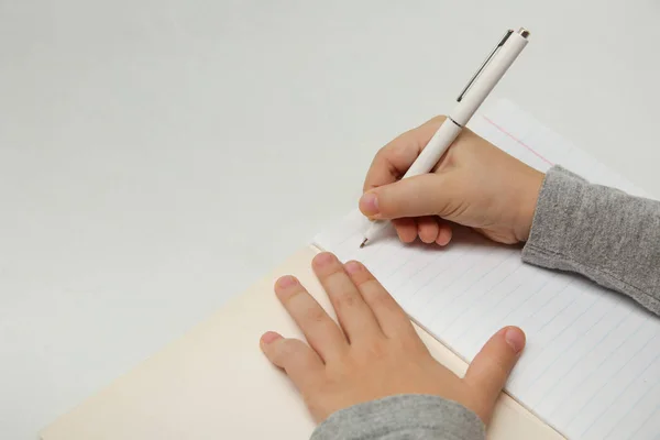 Çocuğun eli beyaz arka planda bir defter yazıyor. Çocuk ilk harfleri yazar. Beyaz arka planda bir çocuğun elinde beyaz kalem.