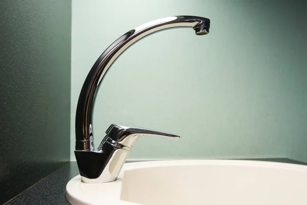 Single-handle tap in the kitchen. white kitchen sink on dark countertop. chrome-plated mixer tap with single handle.