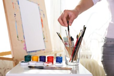 Sanatçının eli sehpada kağıt üzerinde bir fırçayla çizer.