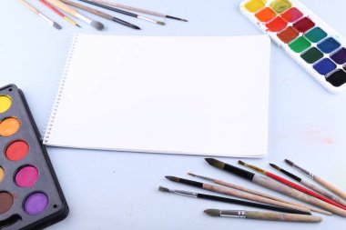 Boya fırçaları, boyalar ve kâğıtlar masanın üstünde, üst tarafta.