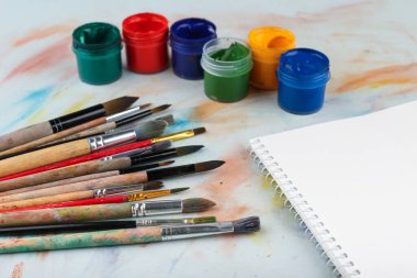 Boya fırçaları, boyalar ve kâğıtlar masanın üstünde, üst tarafta.