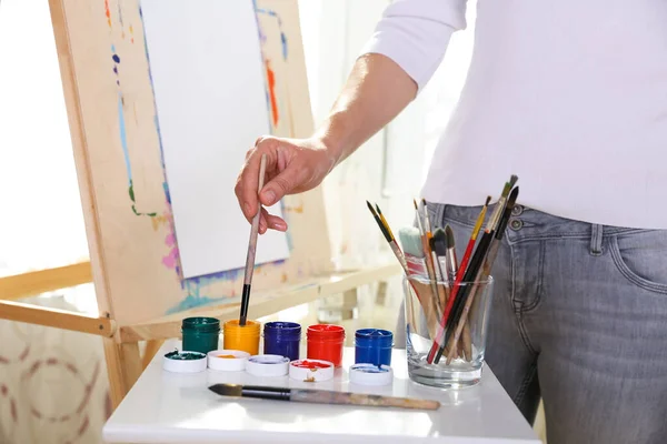 the artist\'s hand draws with a brush on paper on easel