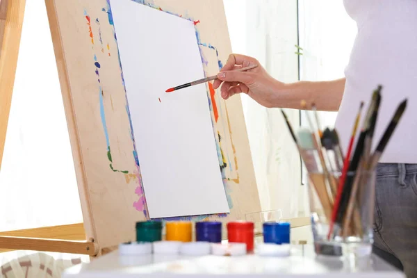 the artist\'s hand draws with a brush on paper on easel