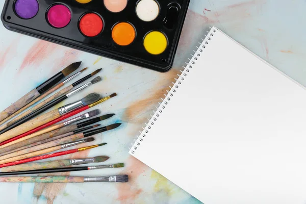 Boya fırçaları, boyalar ve kâğıtlar masanın üstünde, üst tarafta.