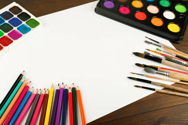 Boya fırçaları, boyalar ve kâğıtlar masanın üstünde, üst tarafta.