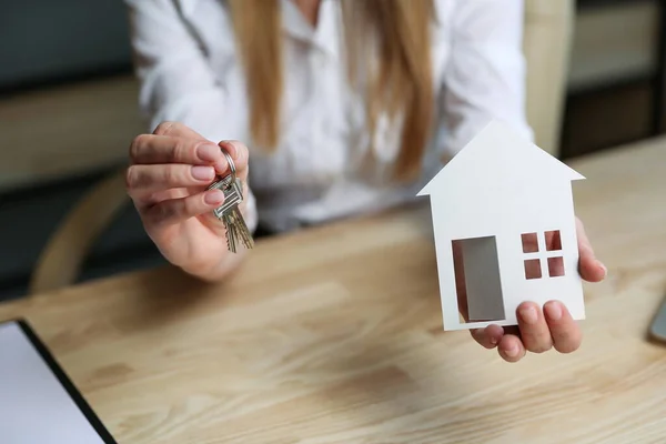 Ev dekorasyonu konsepti. Emlakçının elleri evin anahtarlarını ve modelini tutuyor. Gayrimenkul alım satımı işlemi tamamlandı. Konut anahtarlarını yakın plan çekiyoruz. Yaşam alanının genişlemesi