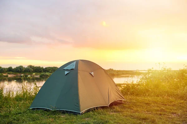 Yeşil turist çadırı gün batımında nehrin kıyısında.