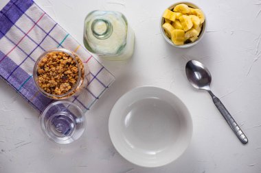 Beyaz bir tabloda bir cam kavanoz ev yapımı musli süt olgun muz beyaz arka plan ile dilimlenmiş kahvaltı zamanı. Düşey yönde boşaltmak flait lay