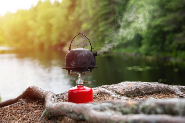 Making tea in the forest. Lake and forest on background. Camping concept.